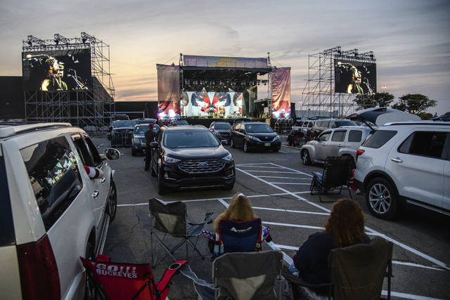 <p>FILE - Attendees sit next to their car as J.R. Moore & Zack Mack perform at the Drive-In at Westland Mall in Columbus, Ohio on Oct. 10, 2020. After a historic season, winter is coming at the drive-in. Summer and early fall have seen the old drive-in transformed into a surprisingly elastic omnibus of pandemic-era gathering. It has hosted concerts and comedy shows, business conferences and Sunday services, graduations and weddings. Drive-ins in Texas, California and Florida can keep humming all year but most of the U.S.’s roughly 300 drive-ins are seasonal. They aren’t built for the cold, and they’re definitely not built for the snow. (Amy Harris/Invision/AP, File)</p>